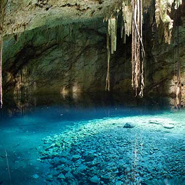 A turquoise pool of water shimmers in a cave. The color is caused by finely ground minerals suspended in the water.