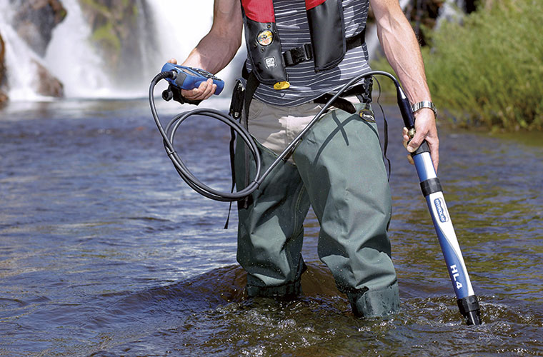 A hydrologic technician spot checking water quality in a stream with a HYDROLAB HL4 and surveyor.