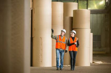 Two workers walking among paper rolls