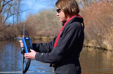 Woman using an OTT MF Pro flow meter to measure depth and velocity in a stream