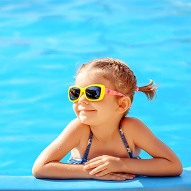 A young child smiles at the edge of a pool. Water hardness in pools can damage pool surfaces and corrode pipes.