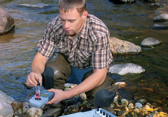 A water quality professional using a Hach handheld colorimeter near a stream.